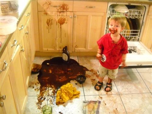 toddler boy with chocolate pudding all over himself and kitchen floor